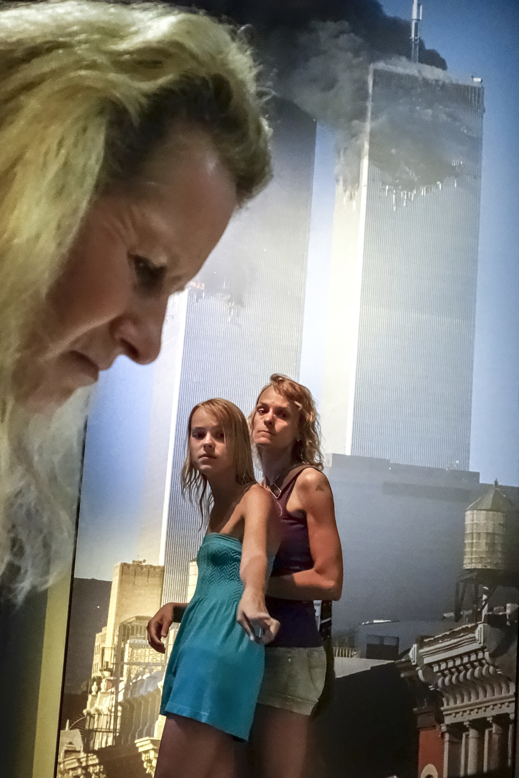 two women stand in front of a giant blown up photograph of the Twin Towers