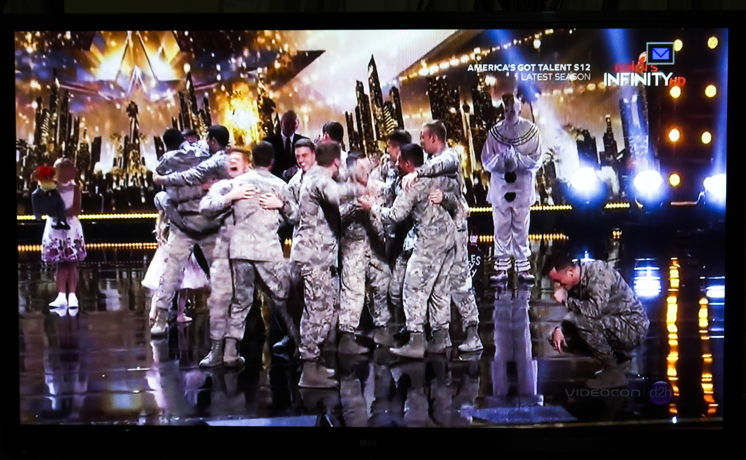 A television screen with a group of men all hugging each other in combat fatigues