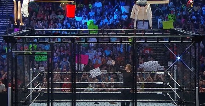 A black cage surrounding a wrestling ring with all kinds of items (mop, straitjacket, leather strap) dangling above.