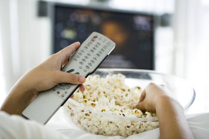 Someone holds a remote while watching a movie with a big bowl of popcorn