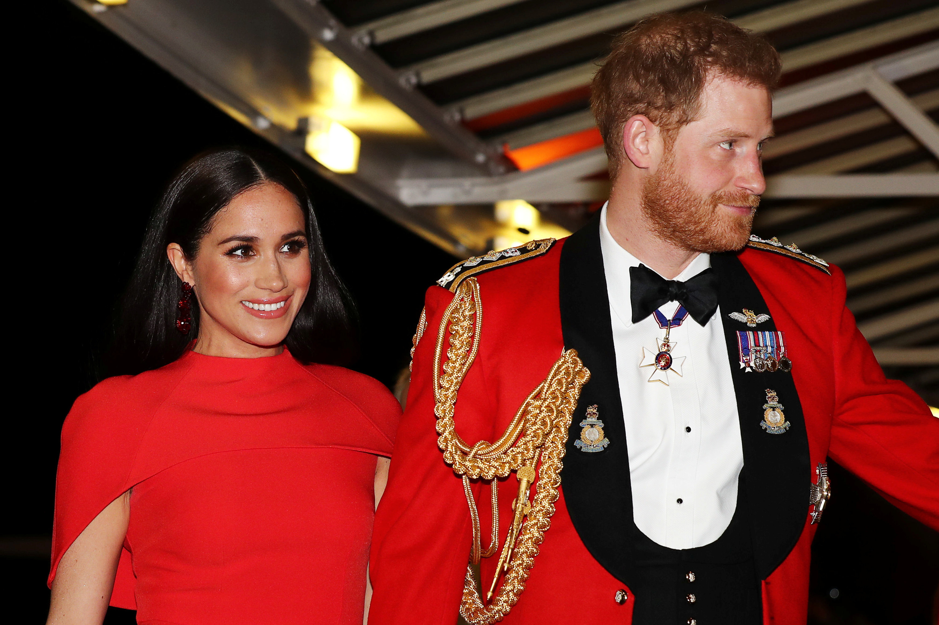 Meghan smiles in a red dress at a formal event with Harry