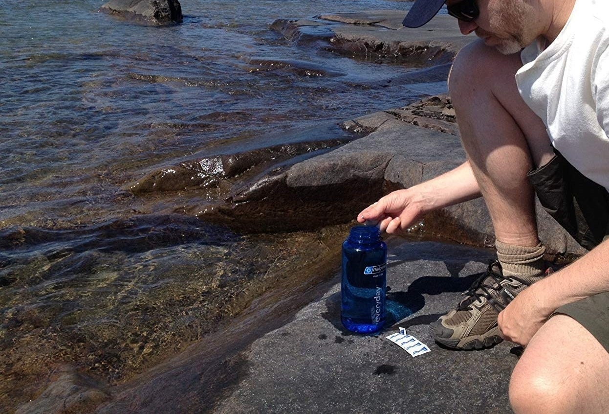 A person filling up their nalgene water bottle next to a packet of water purification tablets 