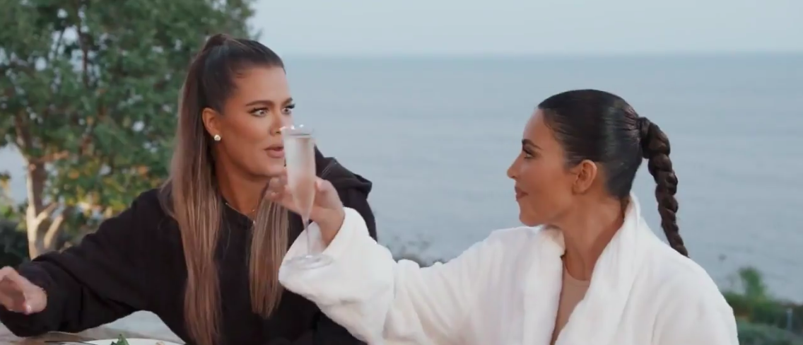 Kim holds up a champagne glass while Khloé looks on