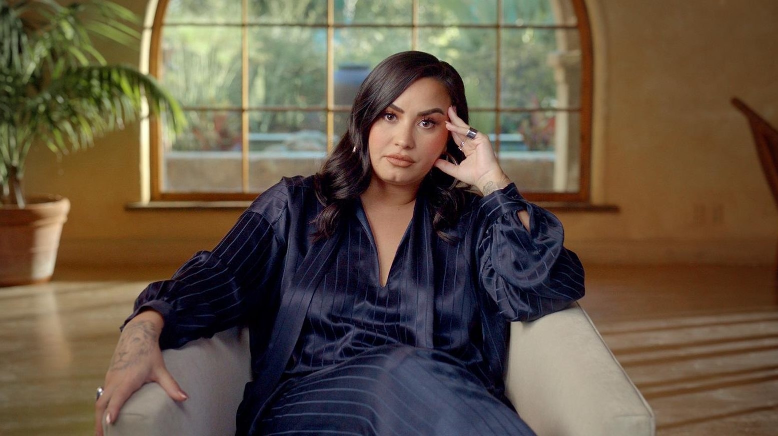 Lovato sitting in a chair, looking seriously at the camera