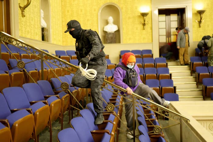 A masked man and woman climb over a railing amid rows of seats