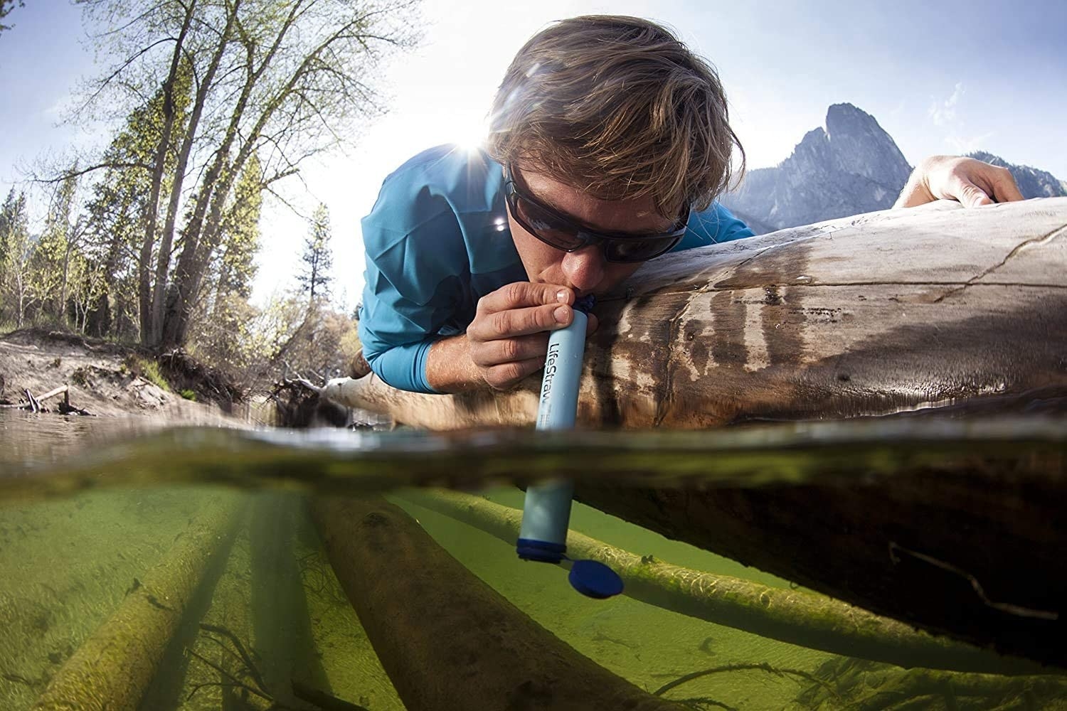 model drinks from blue LifeStraw Personal Water Filter placed in a stream