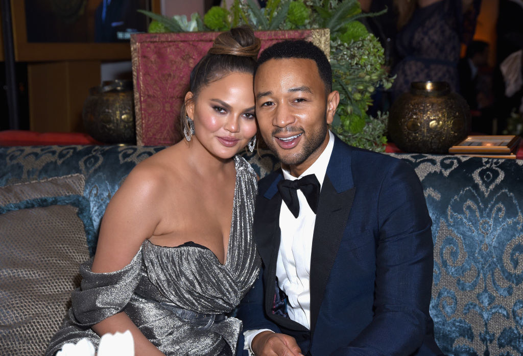 Chrissy and Teigen sitting on a couch together cheek to cheek