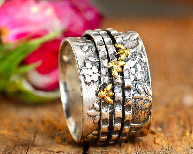 Silver band ring with floral details and three thin spinner rings with bright bee details 