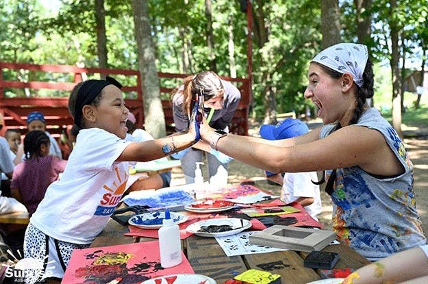 Camper and counselor high-fiving over craft table.