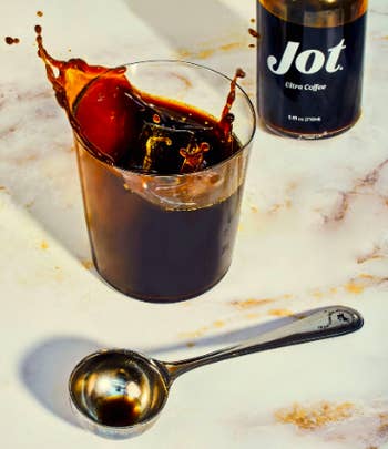 Glass of coffee beside bottle of product and serving spoon 