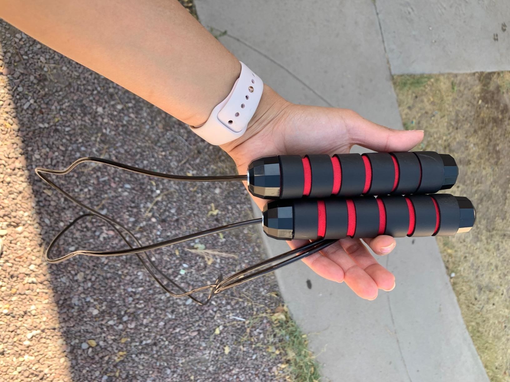 reviewer holds black and red jump rope in hands over sidewalk