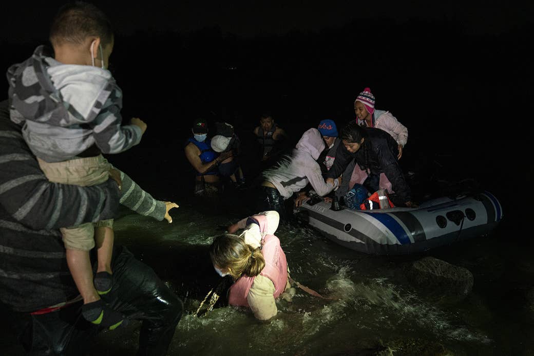 A woman lies in river rapids between her husband, who holds a young chlid and reaches out for her, and an inflatable raft carrying asylum-seekers