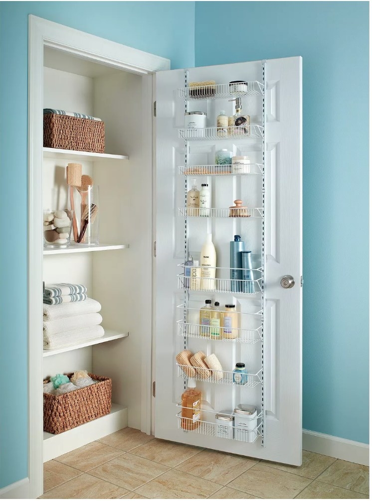 An 8 tier over-the-door adjustable wire rack in white filled with linen closet products such as soaps, sponges, shampoos, etc 