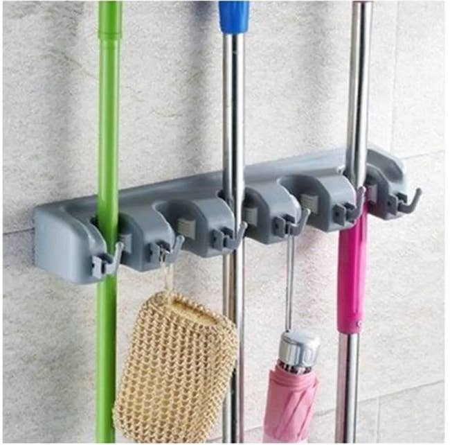 A wall-mounted, cleaning supplies organizer with 5 adjustable brackets to hold various items such as brooms, mops, and more securely in place