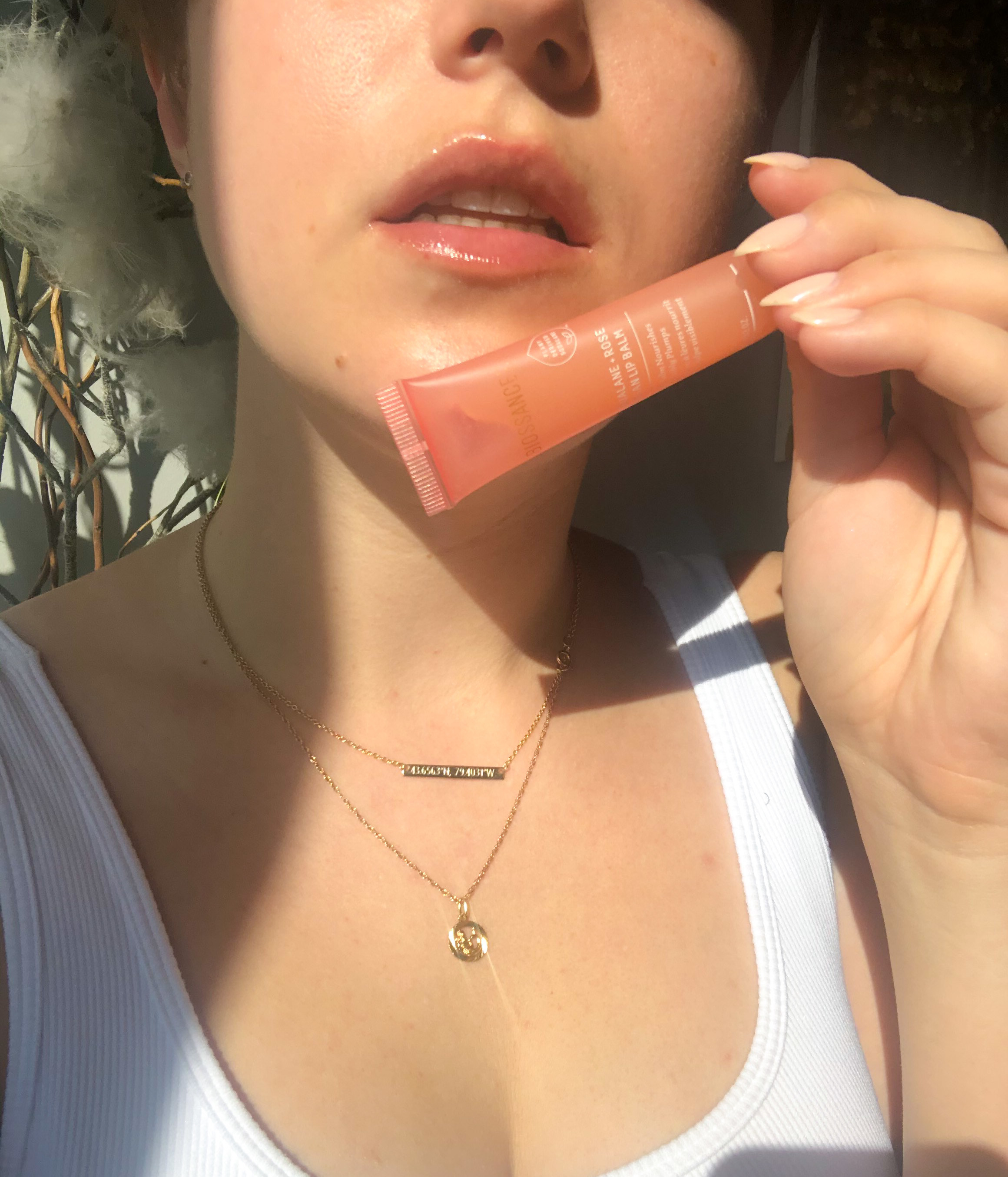 A person holding up a tube of the lip balm to their glossy lips