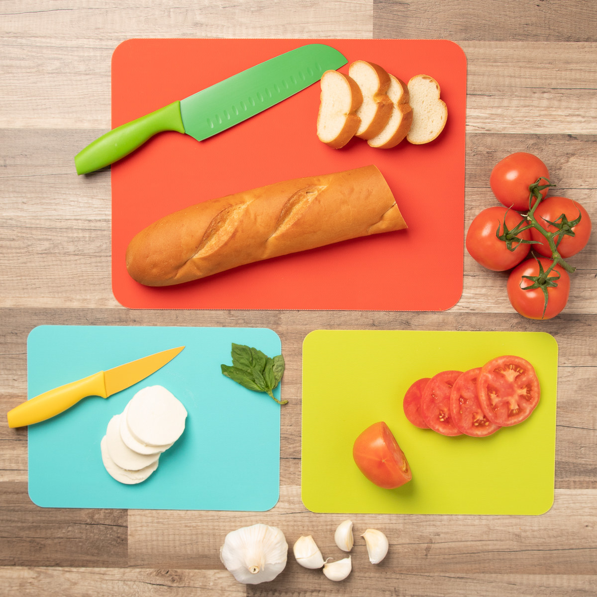 a large orange and small teal and green cutting boards on a counter with bread, tomatoes, garlic, and cheese