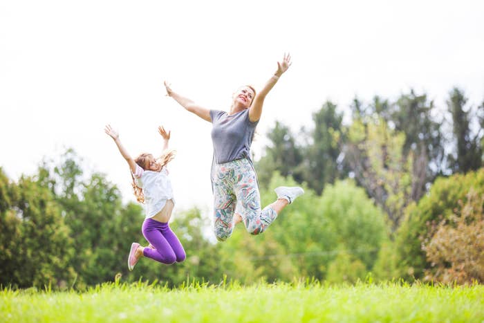 A mother and daughter are outside, jumping for joy.