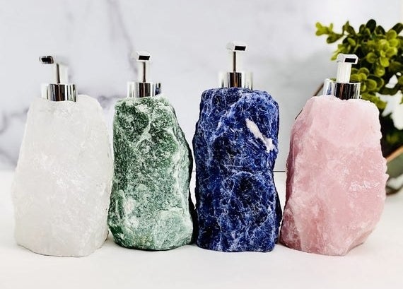 four different-colored rough-cut stone soap dispensers with stainless steel pump tops 