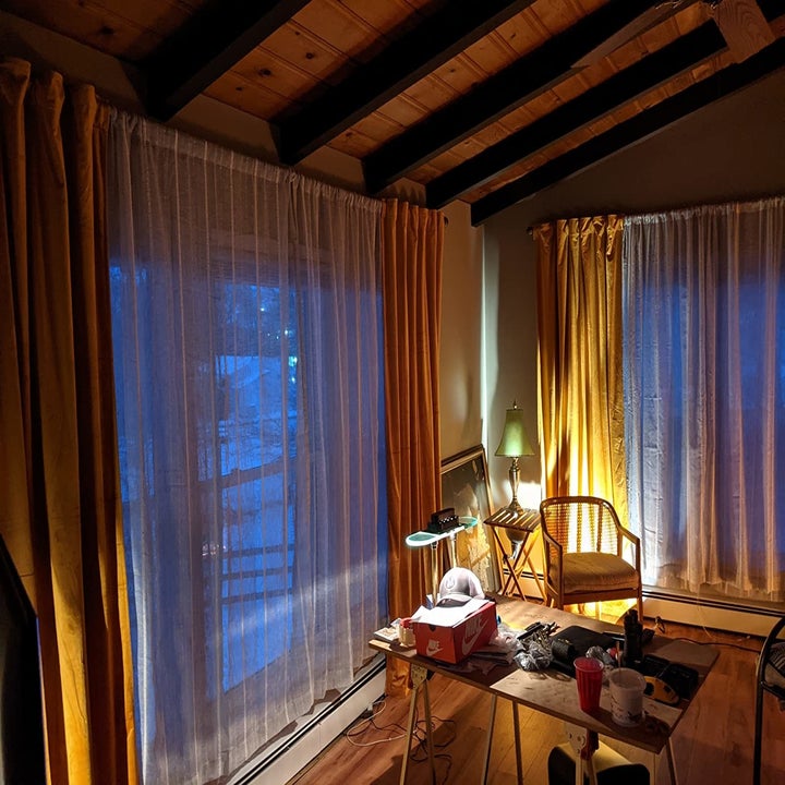 reviewer image of the gold StangH velvet curtains hung up on two floor-to-ceiling windows in a dimly lit living space