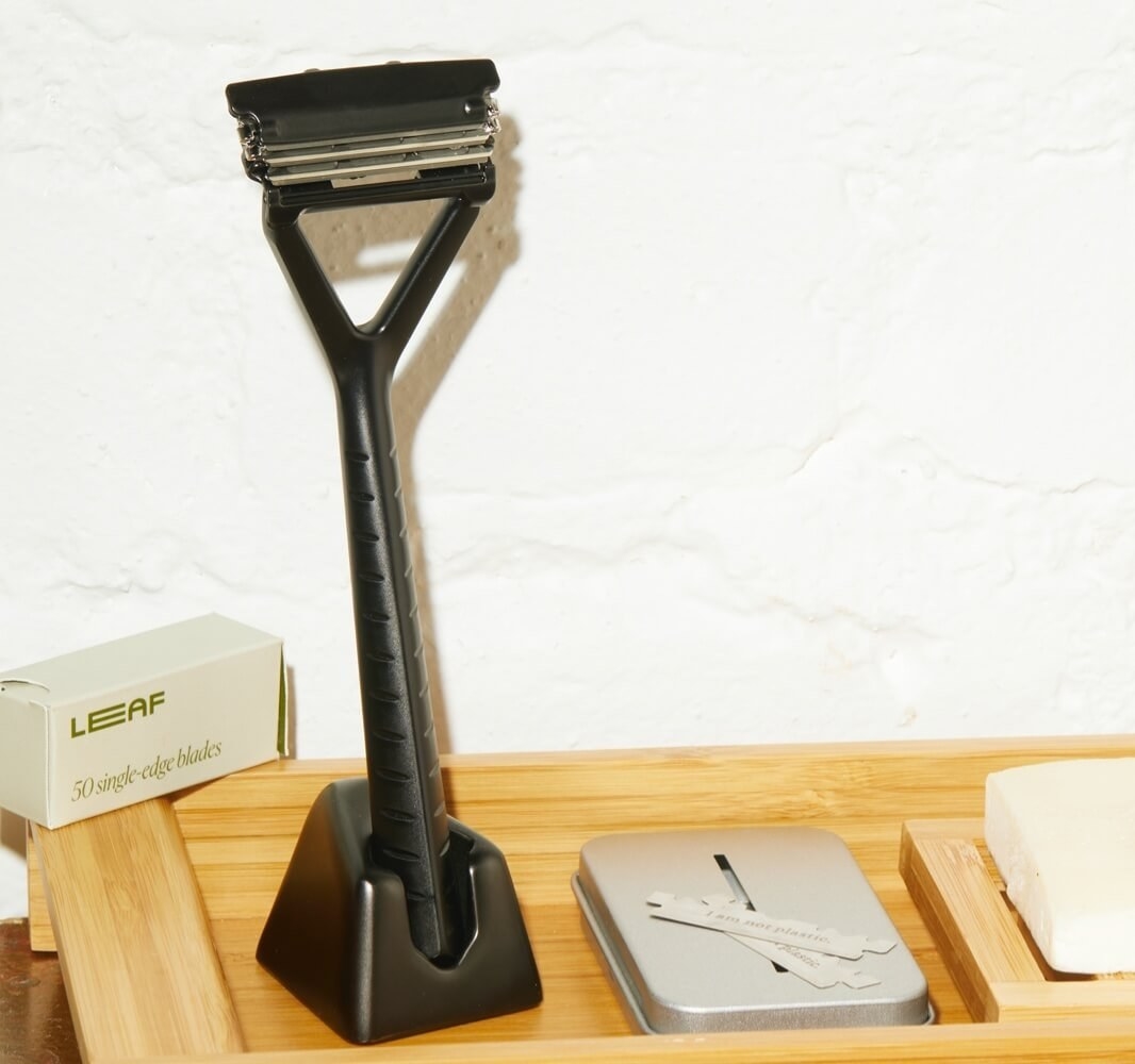a black metal razor in a stand next to a tin and some blades 