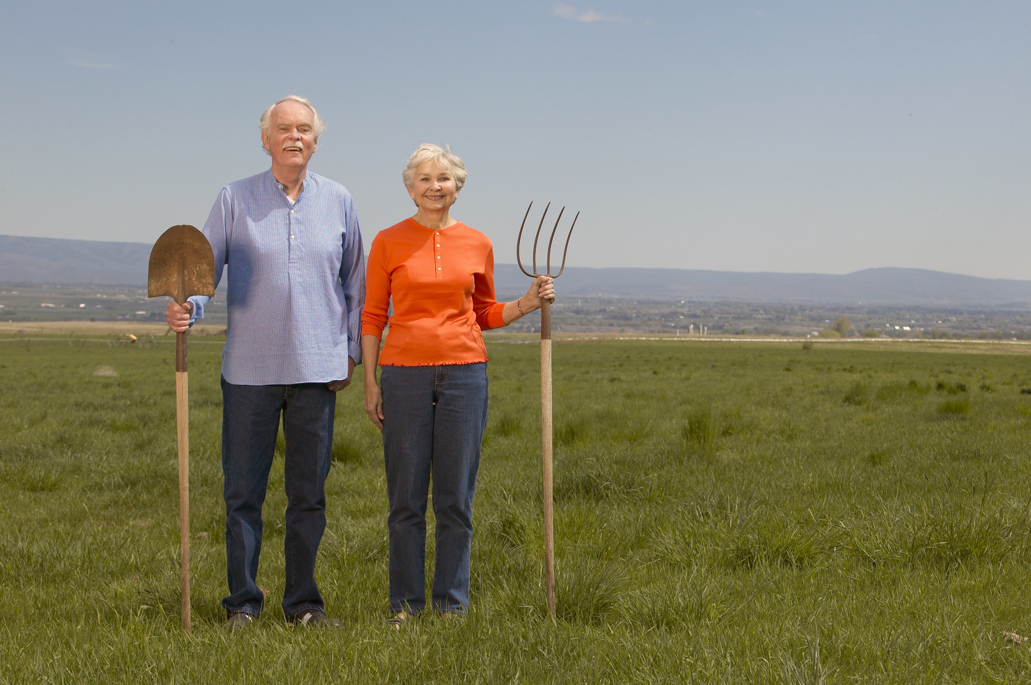 Two people standing in a field holding a shovel and a rake