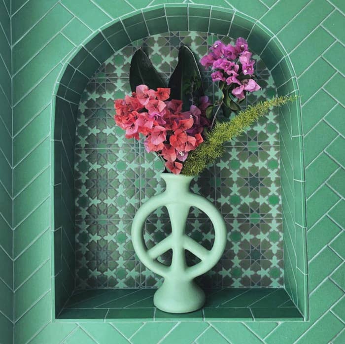 the peace sign-shaped vase in mint with flowers in it 