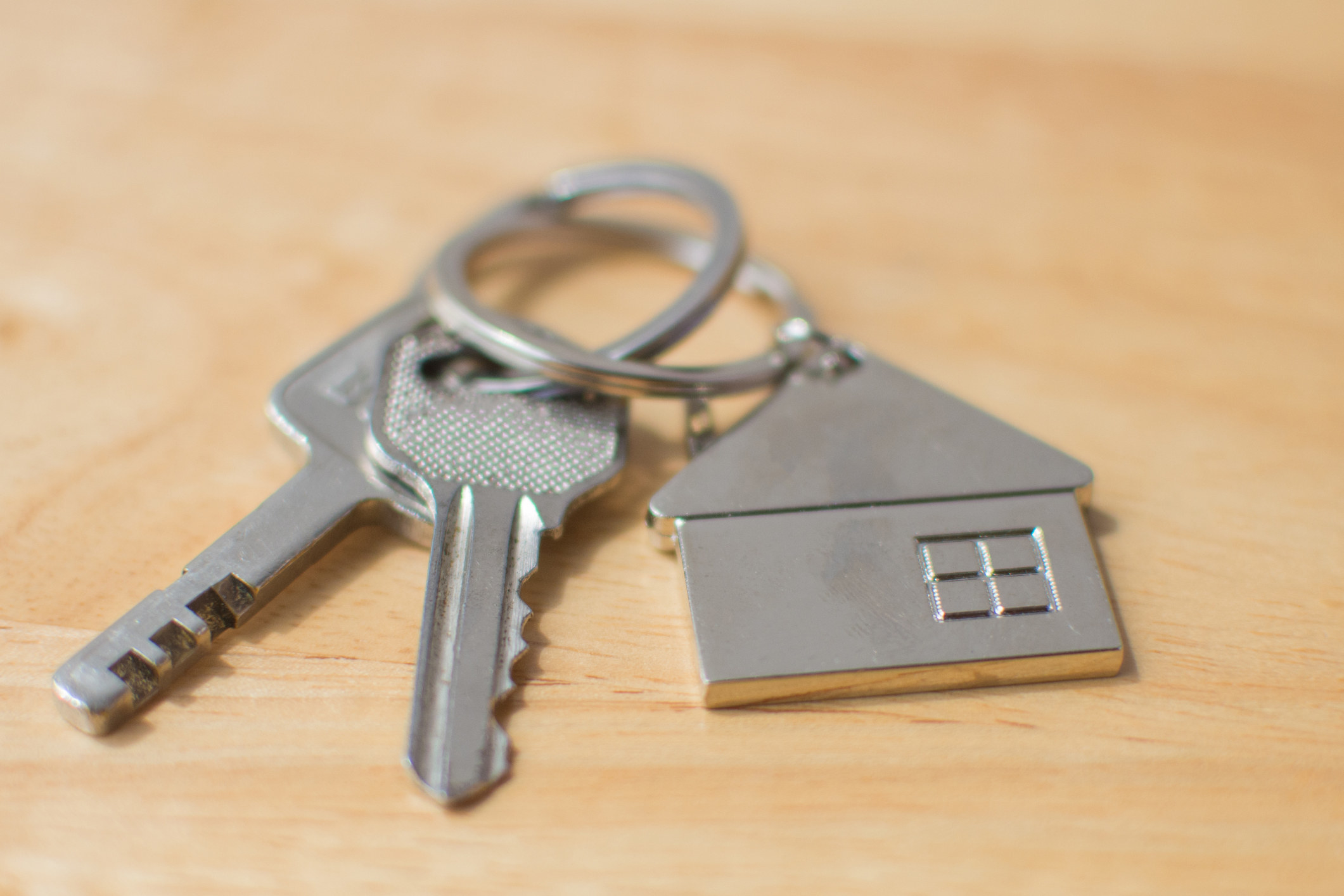 Keys on a home-themed key ring sit on a blonde wood table.