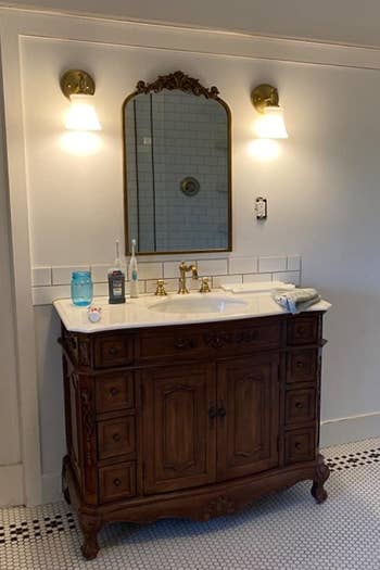a reviewer's gold mirror mounted above a bathroom vanity