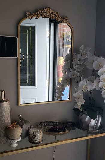 a reviewer with the gold mirror mounted over an entryway table