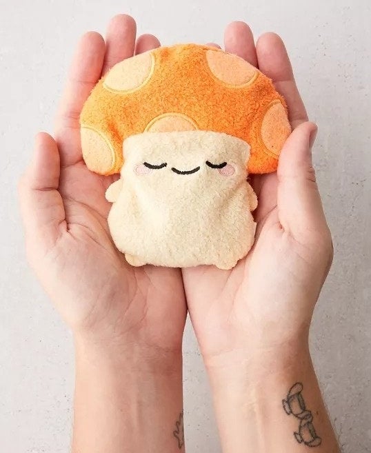 Two hands holding a small mushroom doll heating pad 