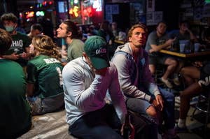 Maskless people crowd together at a bar to watch a football game.