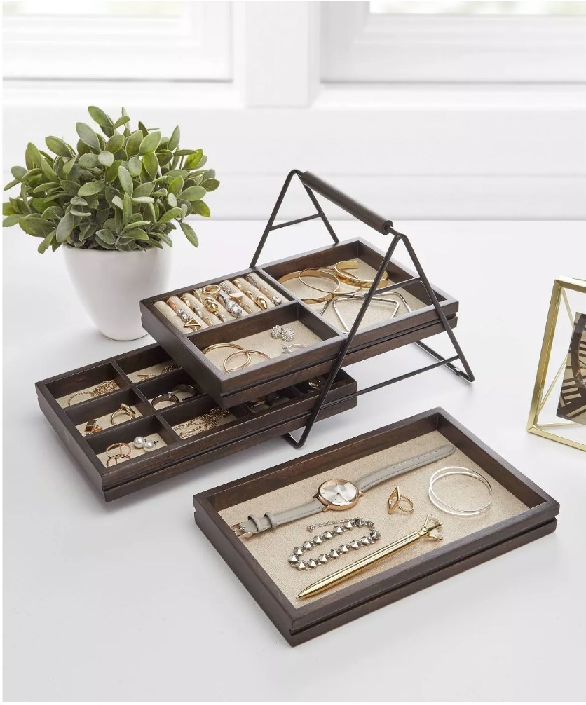 A 3-tier wooden jewelry storage box with linen interiors filled with rings, necklaces, watches, and bracelets