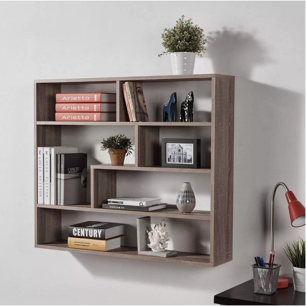 A brown, weathered oak shelf unit mounted to a wall filled with books, plants, and decor items