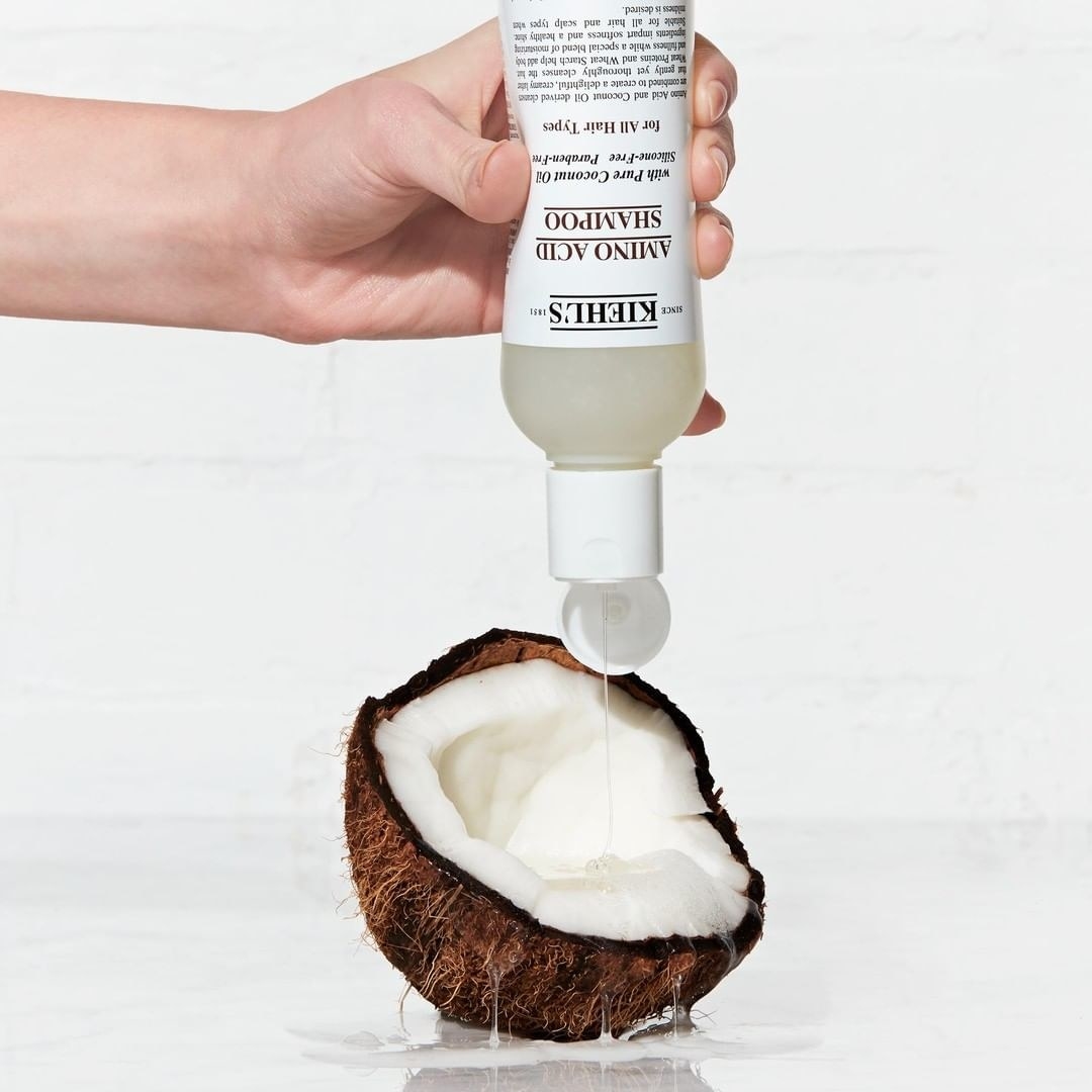 A person pouring shampoo from a bottle into a half cut coconut