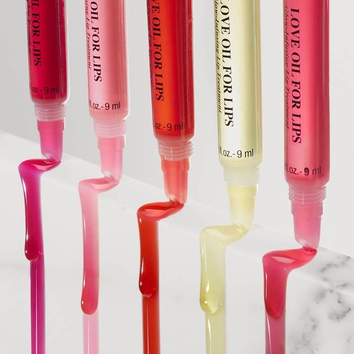 Five tubes of lip oil with their caps on and their contents pouring down a thick marble board