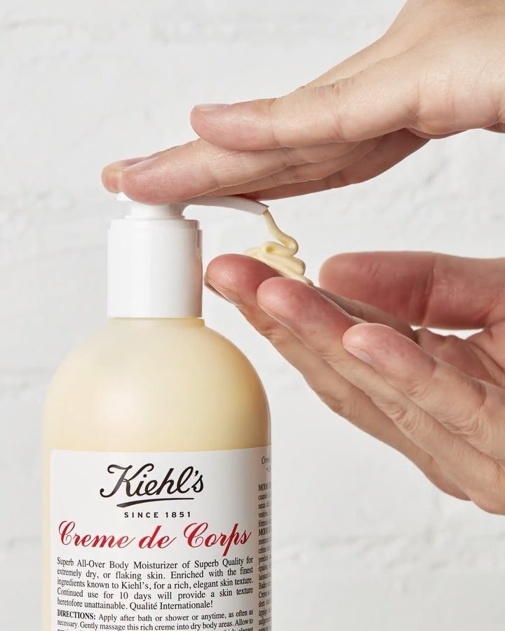 A person dispensing body cream from a bottle into their hand