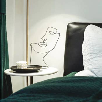 a black wire sculpture in the shape of an abstract face on a nightstand