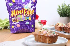 A mini banana loaf with Cadbury Mini Eggs are on top of a plate with some more near by. A bag of Cadbury Mini Eggs is also sitting next to the plate.