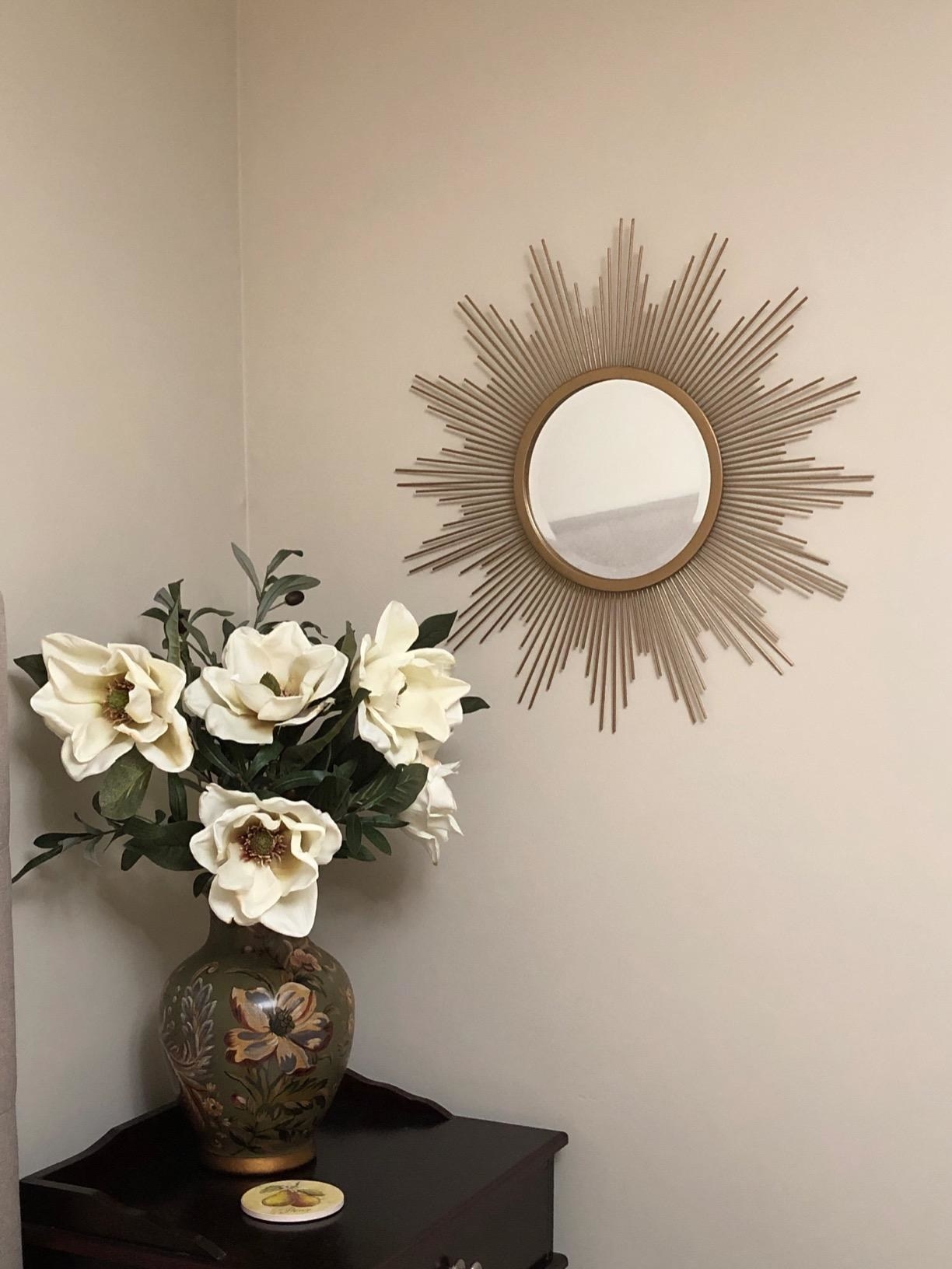 reviewer image of the stonebriar sunburst wall mirror mounted on a wall above a vase full of flowers