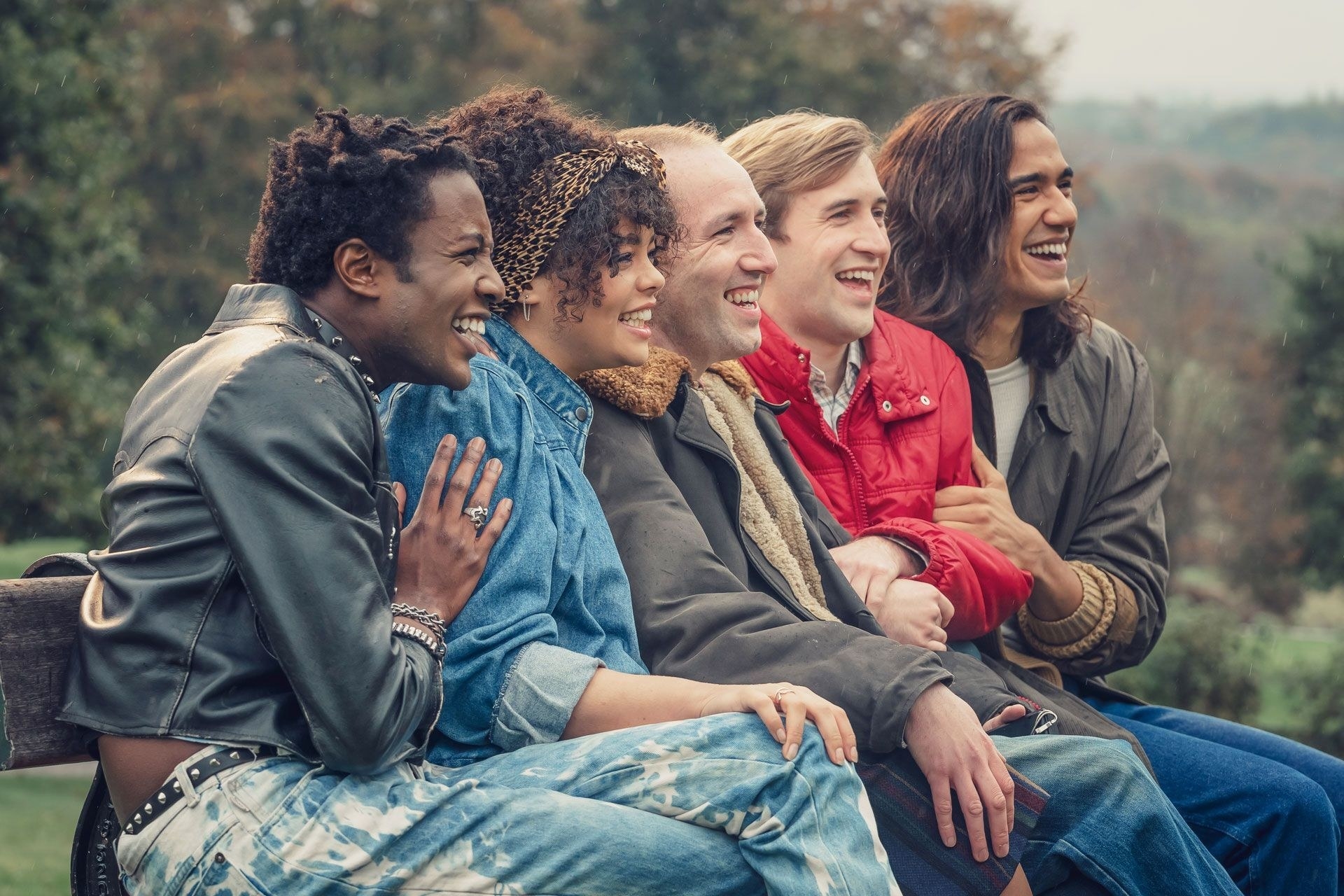 Five friends sit on a park bench and laugh