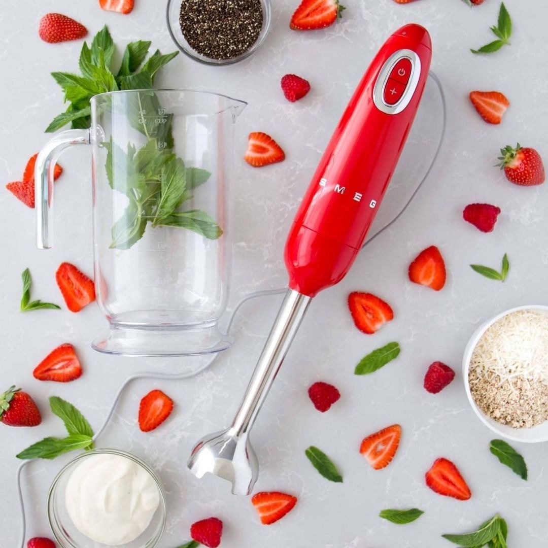 A flatlay of the immersion blender surrounded by cut strawberries and fresh mint leaves