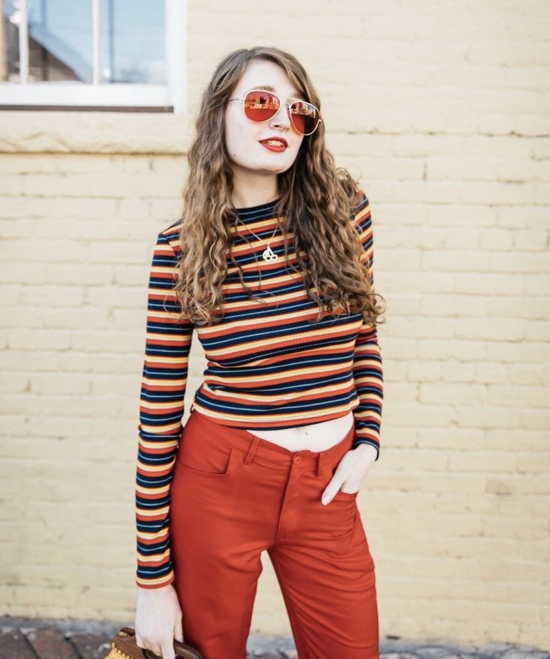 A person wearing a multi-colored striped cropped long-sleeve top and red pants