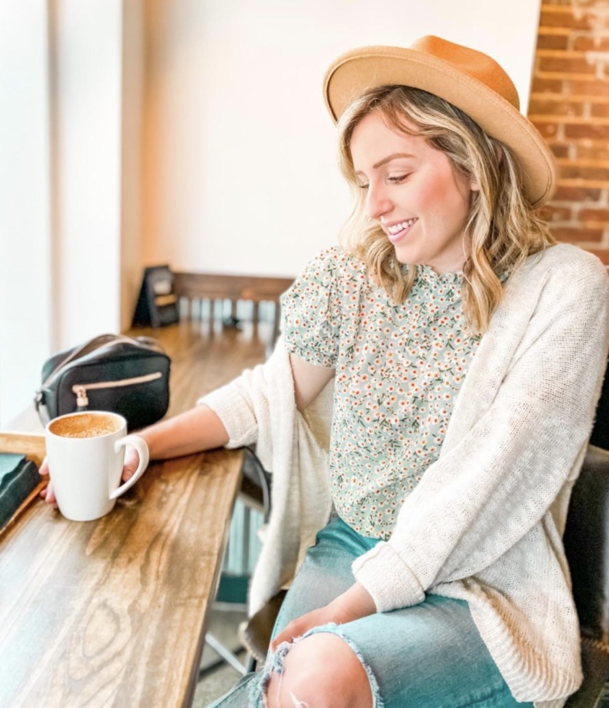 A person wearing a green floral ruffle top, a cardigan, and denim blue jeans