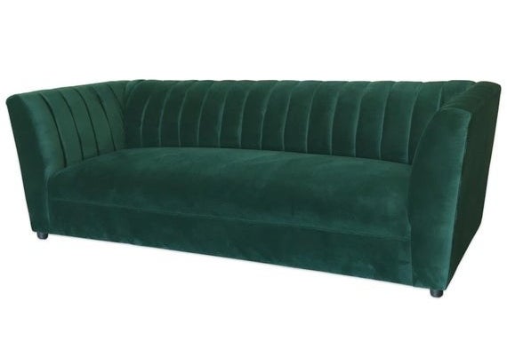 A dark green velvet sofa with angled armrests with channel tufting detailing along the back and sides