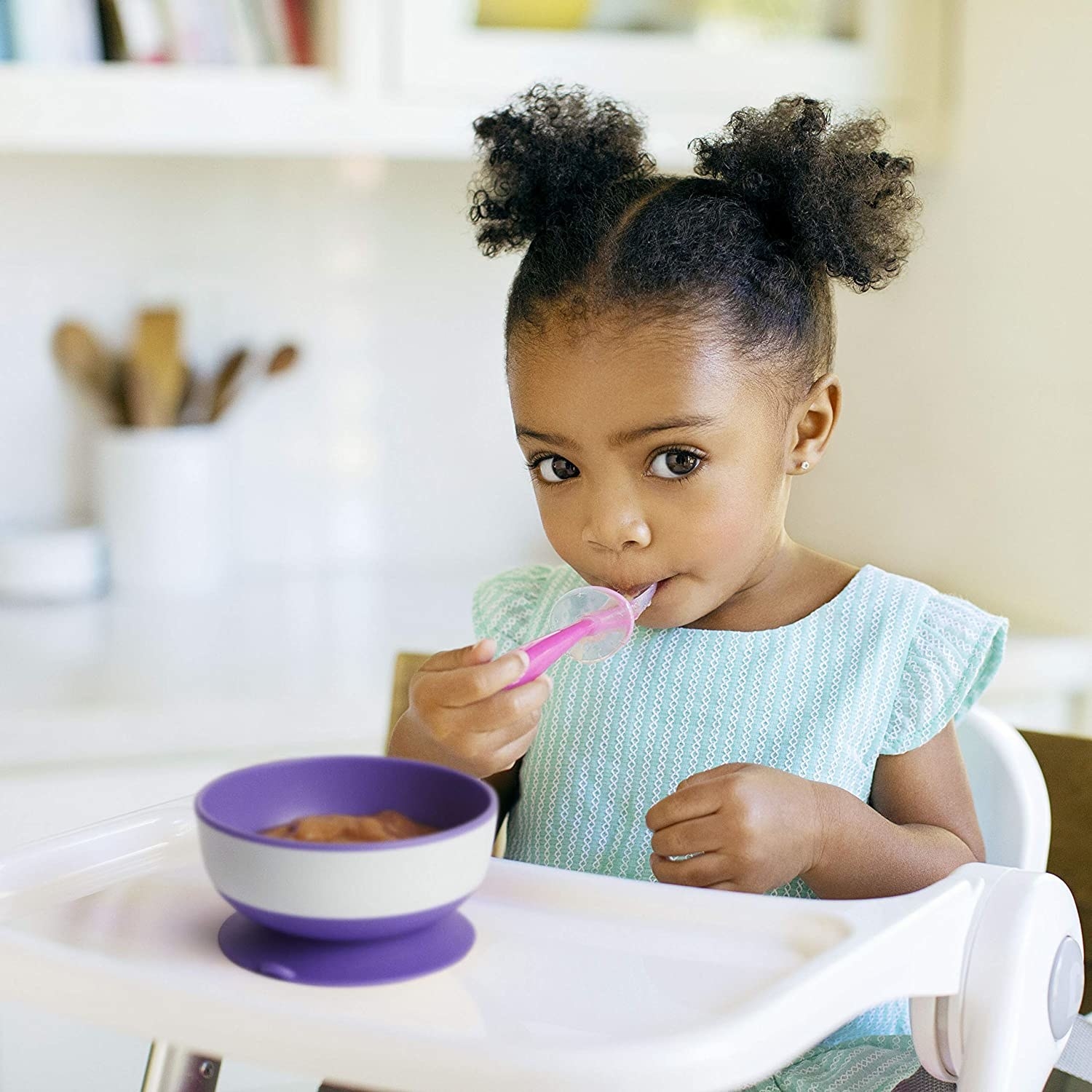 A cute kid eating from the bowl that's suction-cupped to their high chair tray