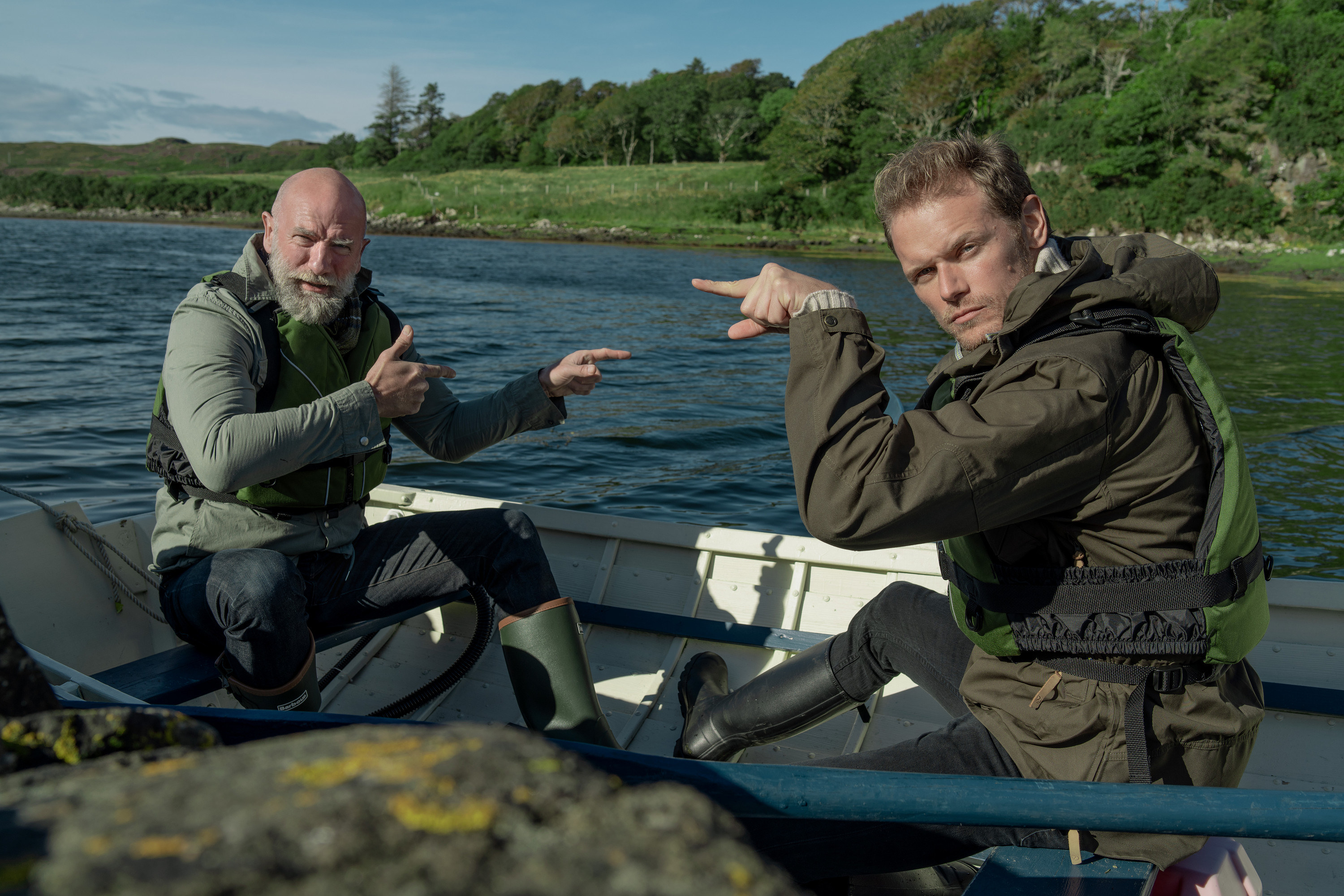 Sam and Graham pointing at one another while sitting in a boat