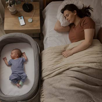 a mom sleeping next to a baby who is in their bassinet with the owlet sock on
