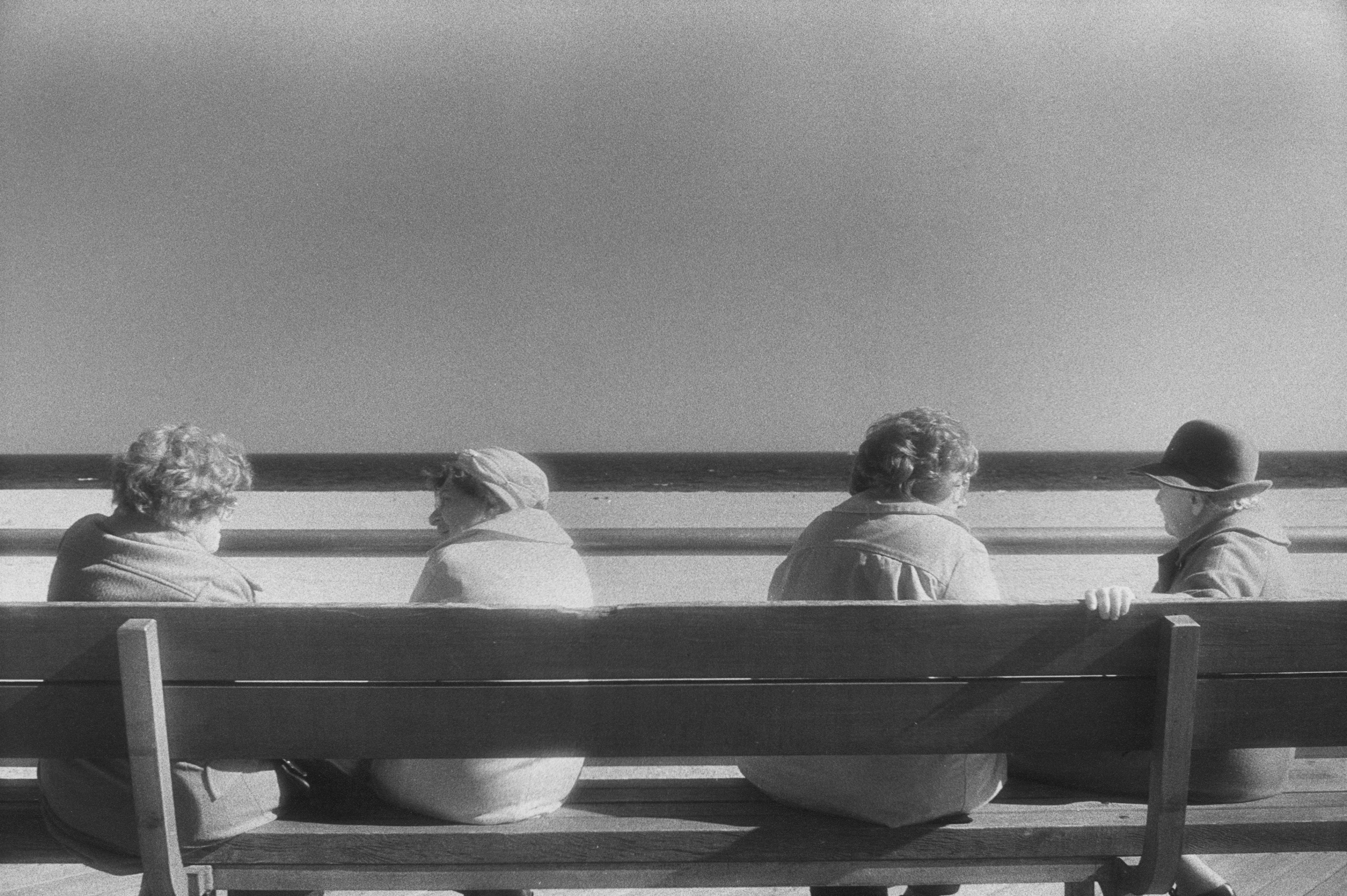 Four older women talking to each other on a bench in front of a beach