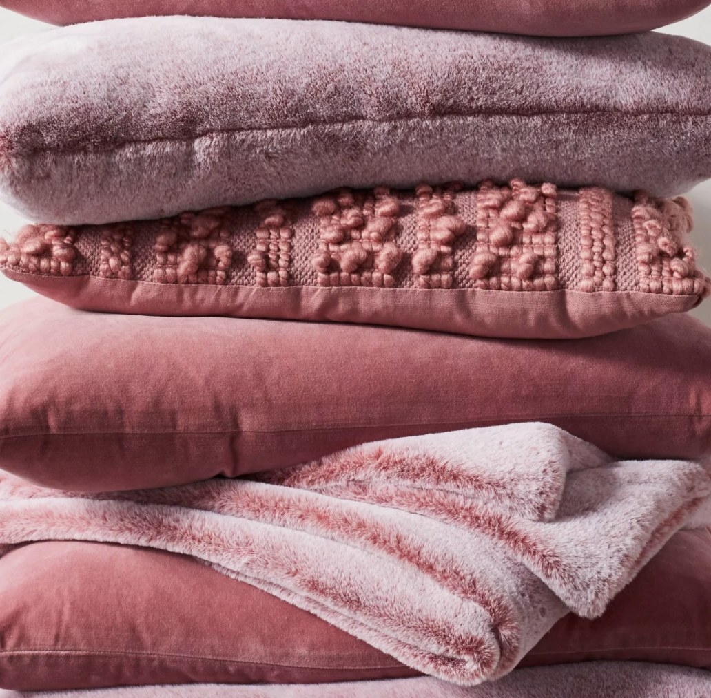 The pillow in pink, stacked amongst blankets and other pillows 