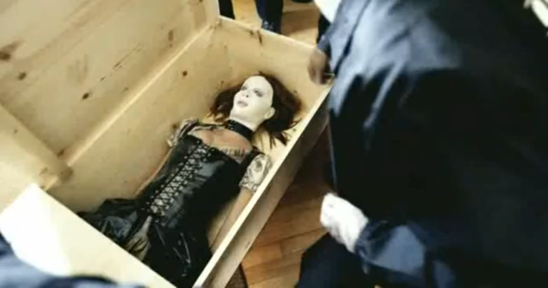 A woman in a mask and leather jacket laying in a box